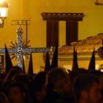 Cruz procesional y nazarenos entre una multitud durante la Semana Santa de Sevilla.
