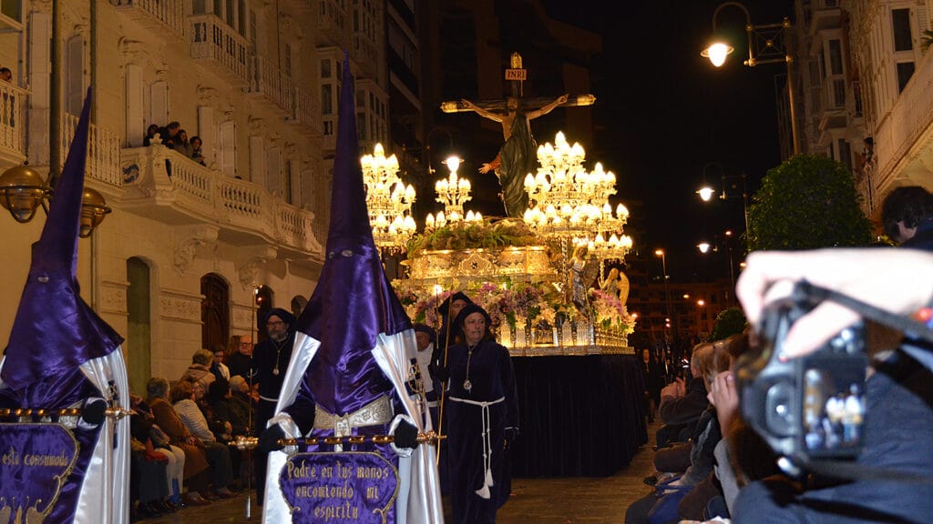 Persona fotografiando entre el público durante una procesión de Semana Santa en Cartagena Prefiero «persona fotografiando» a «fotógrafo trabajando», porque la imagen demuestra que está utilizando una cámara, pero no permite afirmar que se trate de un fotógrafo profesional.