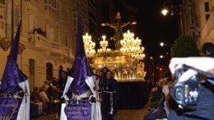 Persona fotografiando entre el público durante una procesión de Semana Santa en Cartagena Prefiero «persona fotografiando» a «fotógrafo trabajando», porque la imagen demuestra que está utilizando una cámara, pero no permite afirmar que se trate de un fotógrafo profesional.