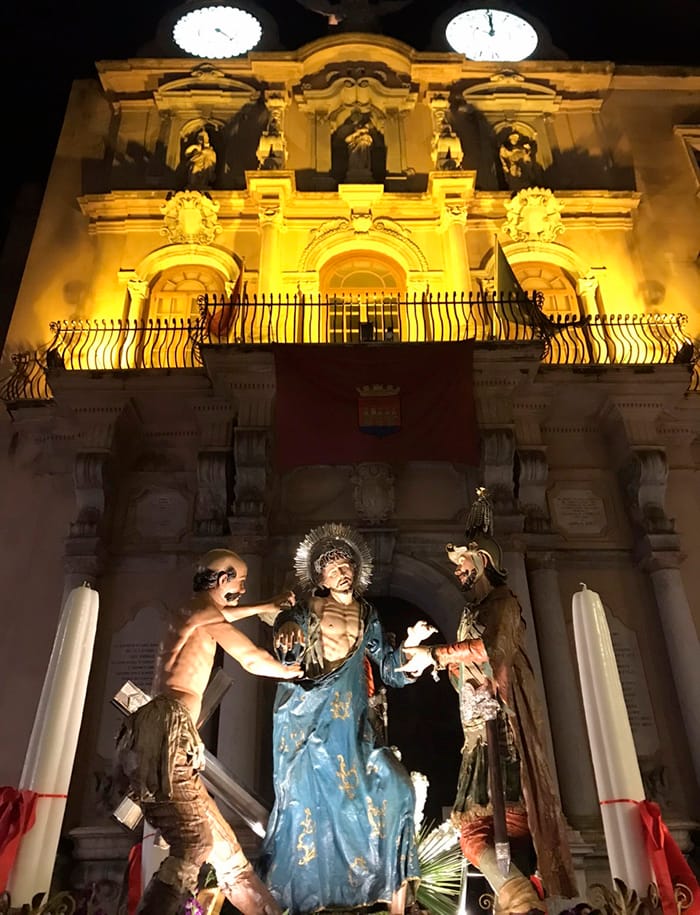 Grupo escultórico de El Expolio ante una fachada iluminada durante la Procesión de los Misterios de Trapani.