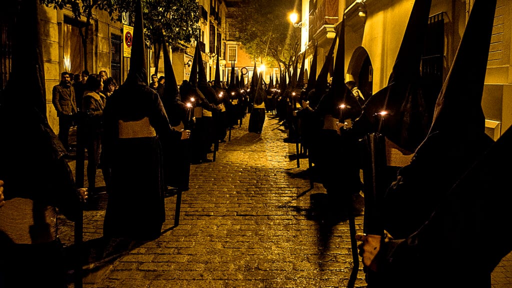 Nazarenos de la Cofradía del Calvario de Sevilla durante la Semana Santa, vestidos con túnicas oscuras.