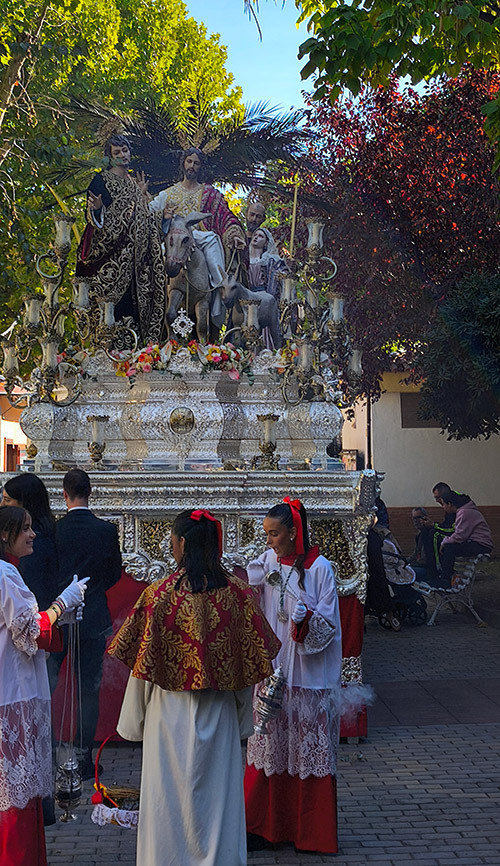 Paso de misterio de Jesús de la Victoria entre los árboles de los jardines de la Estación, con integrantes del cortejo delante.