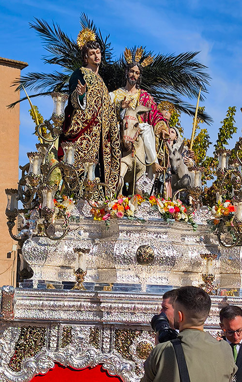 Primer plano del paso de misterio de Jesús de la Victoria, con la orfebrería plateada iluminada por el sol.