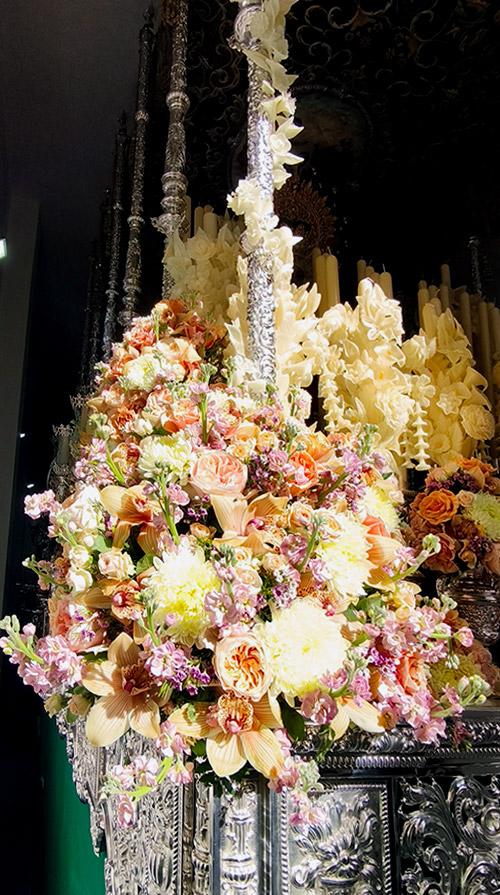 Centro floral del paso de la Virgen del Valle, con rosas de tonos melocotón, orquídeas y flores rosadas y blancas.