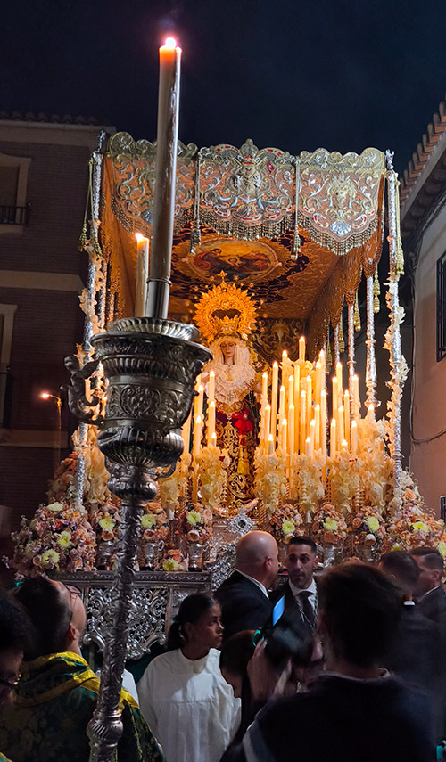 Paso de palio de Nuestra Señora del Valle avanzando de noche por una calle estrecha, acompañado por público.