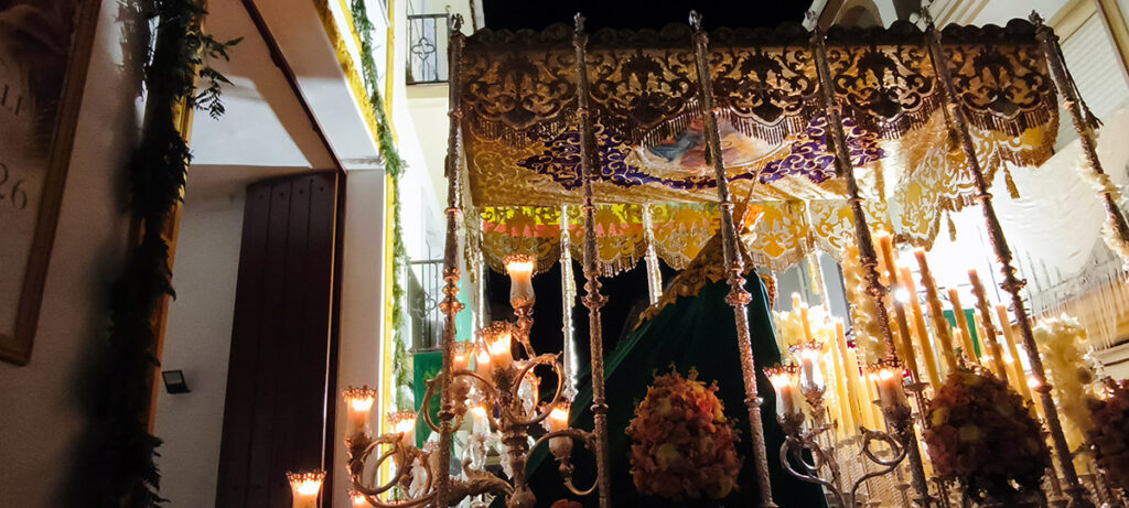 Paso de palio de Nuestra Señora del Valle iluminado por la noche, visto cerca de una fachada y de los espectadores