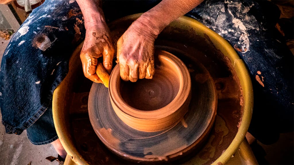 Manos de un artesano modelando una pieza de barro en el torno de alfarero