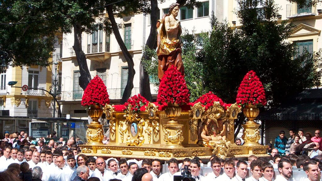 Procesión de Semana Santa entre participantes y público en una calle de Málaga