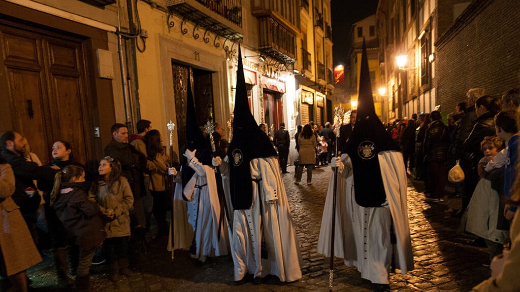 Procesión de Semana Santa recorriendo una calle de Granada entre público y nazarenos.