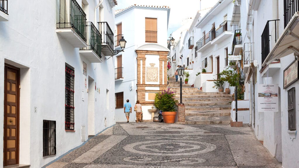 Calle encalada de Frigiliana, con fachadas blancas, balcones, empedrado y escalinata.