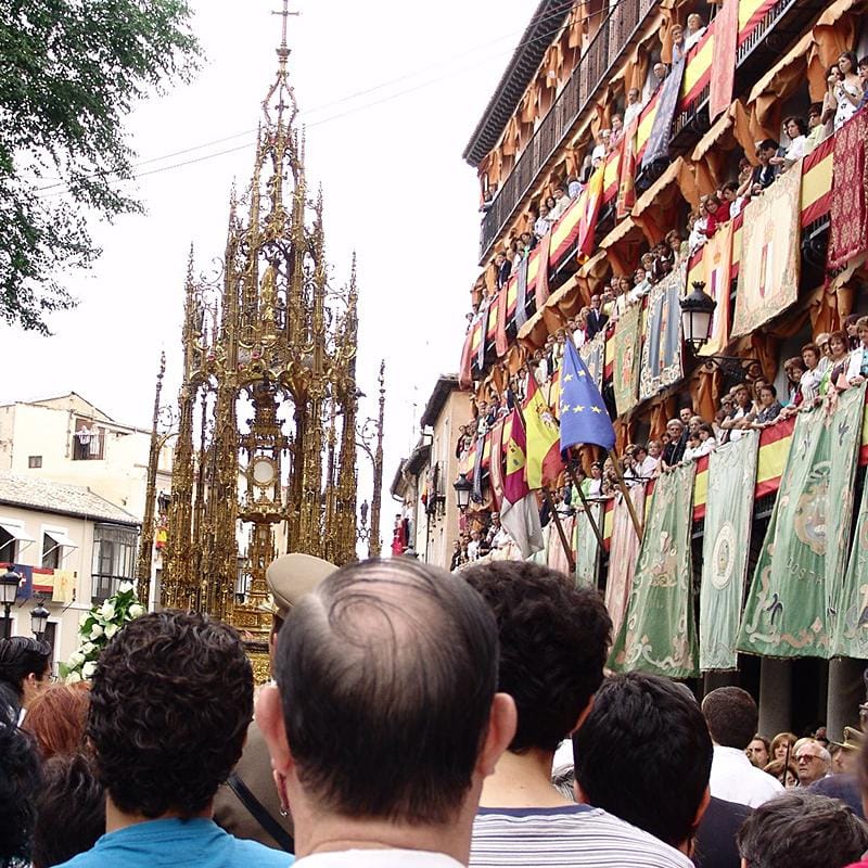 Custodia del Corpus Christi avanzando por una calle de Toledo entre balcones engalanados y espectadores.
