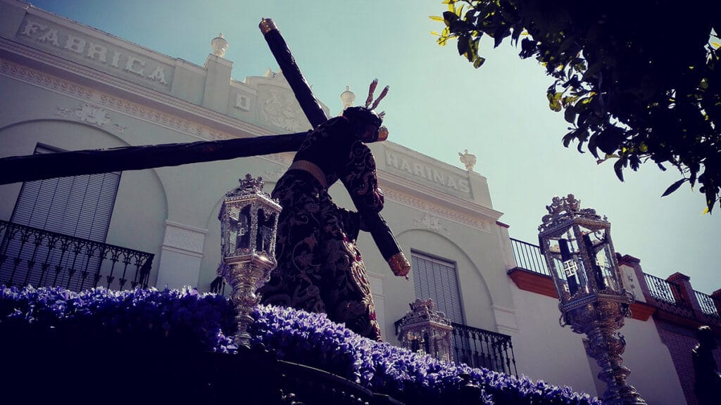 Cristo nazareno en procesión de Viernes Santo en Paradas (Sevilla), con túnica morada y cruz.