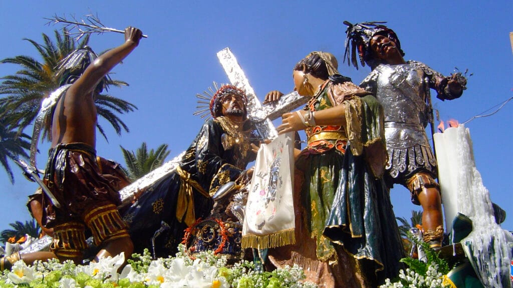 Jesús yacente en urna procesional, acompañado de flores, en la Semana Santa de Trapani.