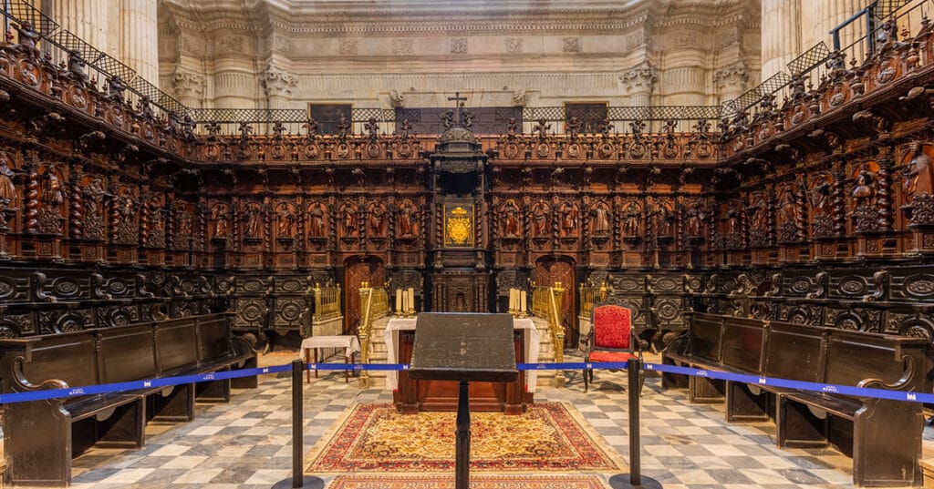 Coro de la Catedral de Cádiz con sillería barroca tallada en madera y altar al fondo.
