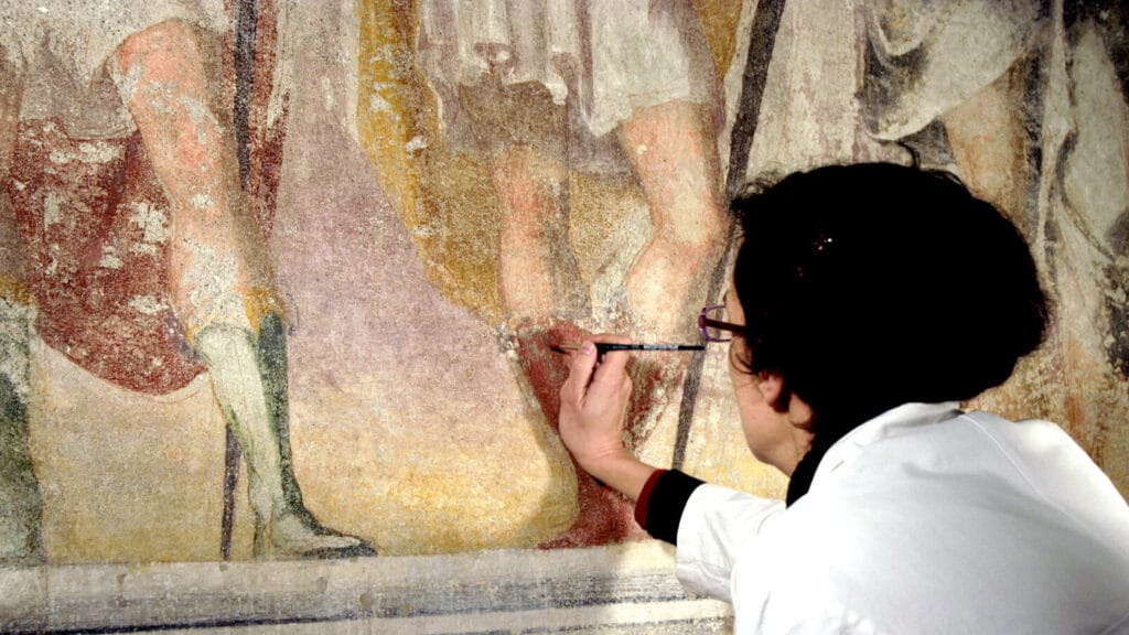 Restauradora trabajando en una pintura mural o fresco en el interior de un templo.