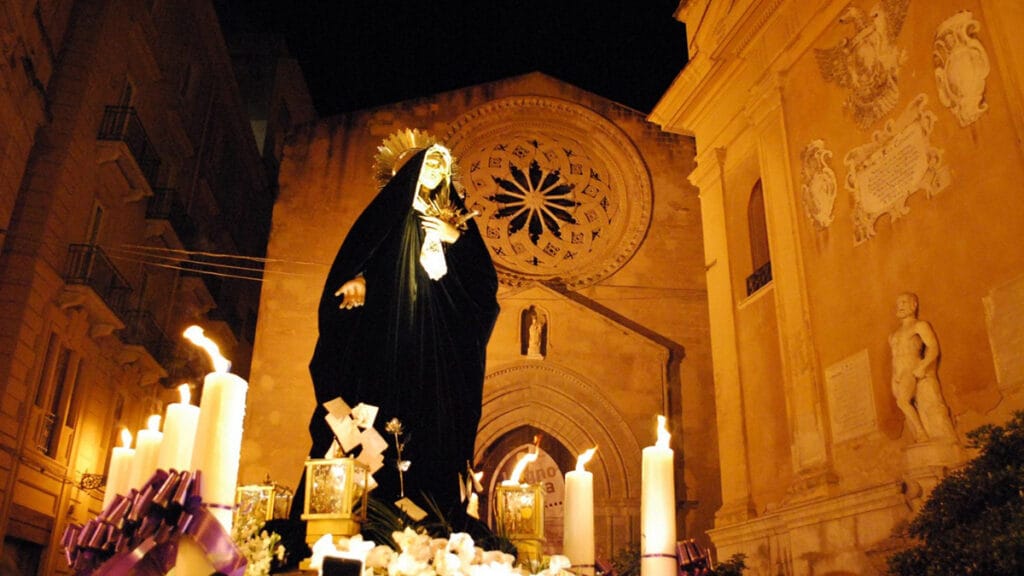 La Virgen Dolorosa (‘Maria SS. Addolorata’) en procesión nocturna, con velas y templo al fondo.