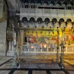La Piedra de la Unción en la Iglesia del Santo Sepulcro, con lámparas votivas colgantes y un gran mosaico al fondo.