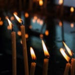 Velas votivas encendidas en un soporte metálico dentro de una iglesia.