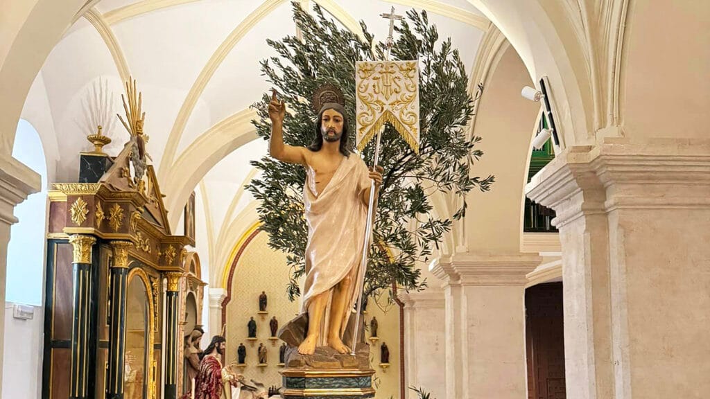 Vista del Señor Resucitado de Padul en el interior del templo, con estandarte, ramas de olivo y arcadas de la iglesia.