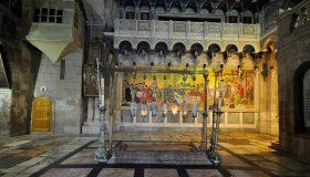 La Piedra de la Unción en la Iglesia del Santo Sepulcro, con lámparas votivas colgantes y un gran mosaico al fondo.