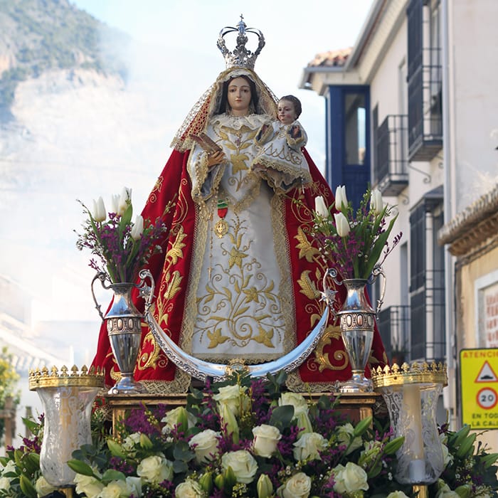 Primer plano de la Virgen de los Remedios con manto rojo y flores blancas en Padul.